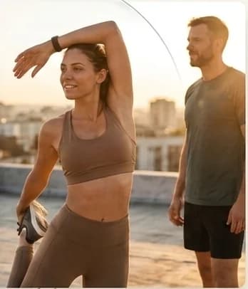 A woman and a man stretching on a rooftop in warm morning light after a run.